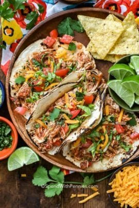 Crock-Pot chicken tacos on a wooden plate with lime wedges and tortilla chips