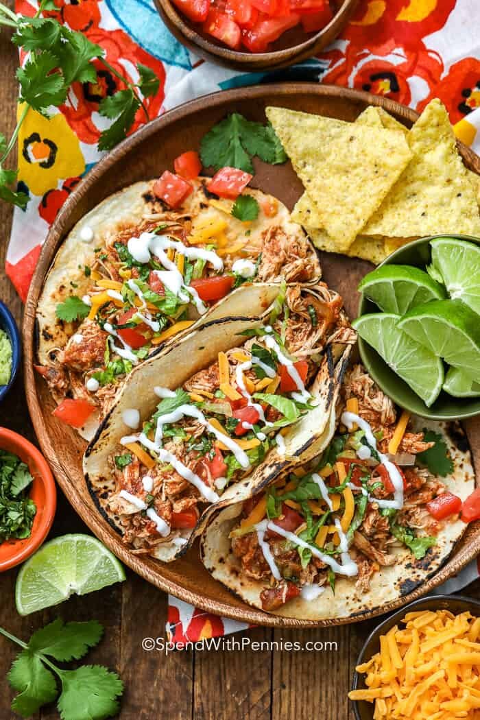 Crock-Pot chicken tacos on a wooden bowl with lime and cheese as garnish