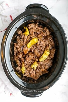 cooked mississippi pot roast shredded in a slow cooker with pepperoncini on top