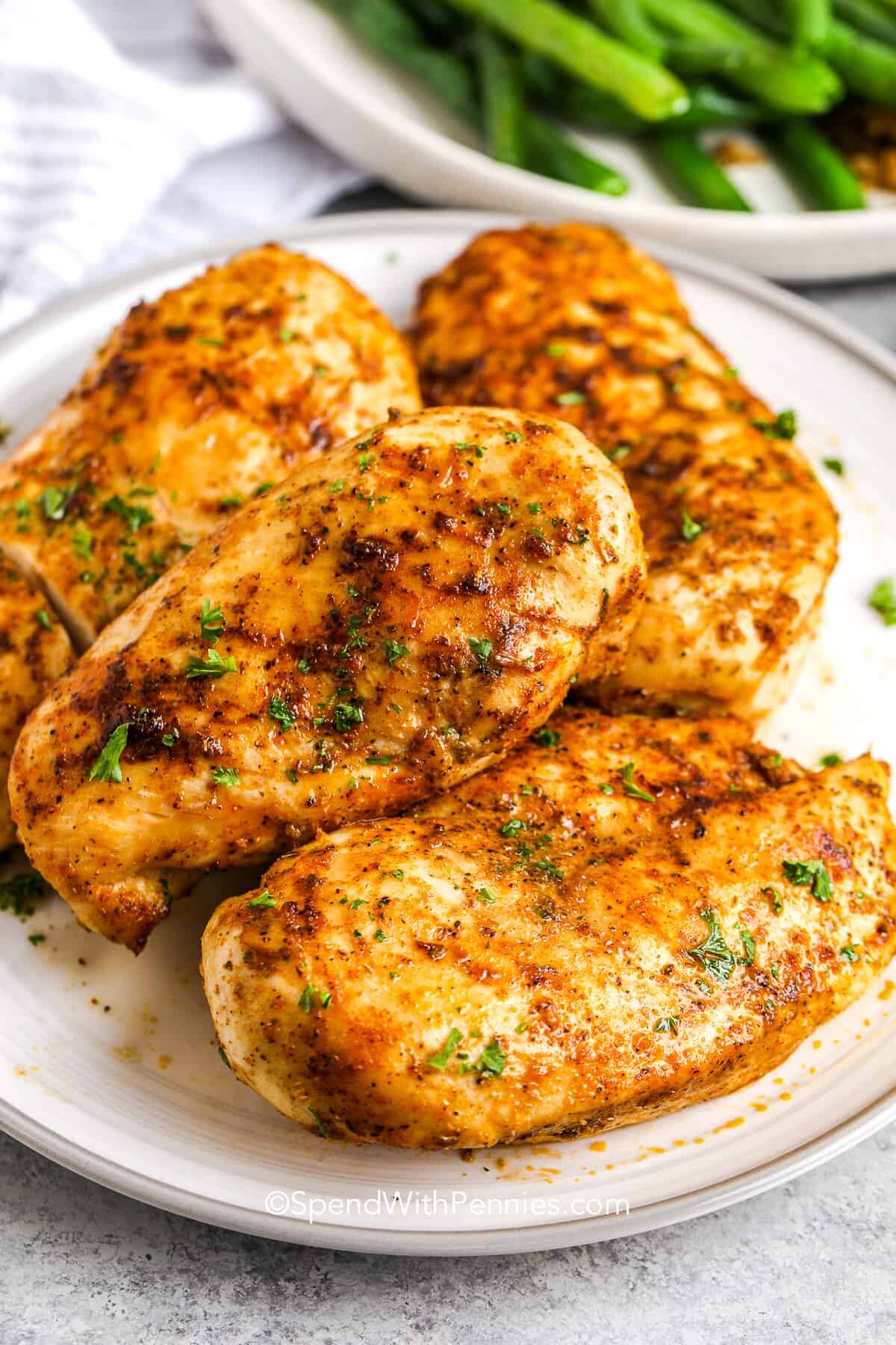 4 air fryer chicken breasts on a plate with green beans in the background