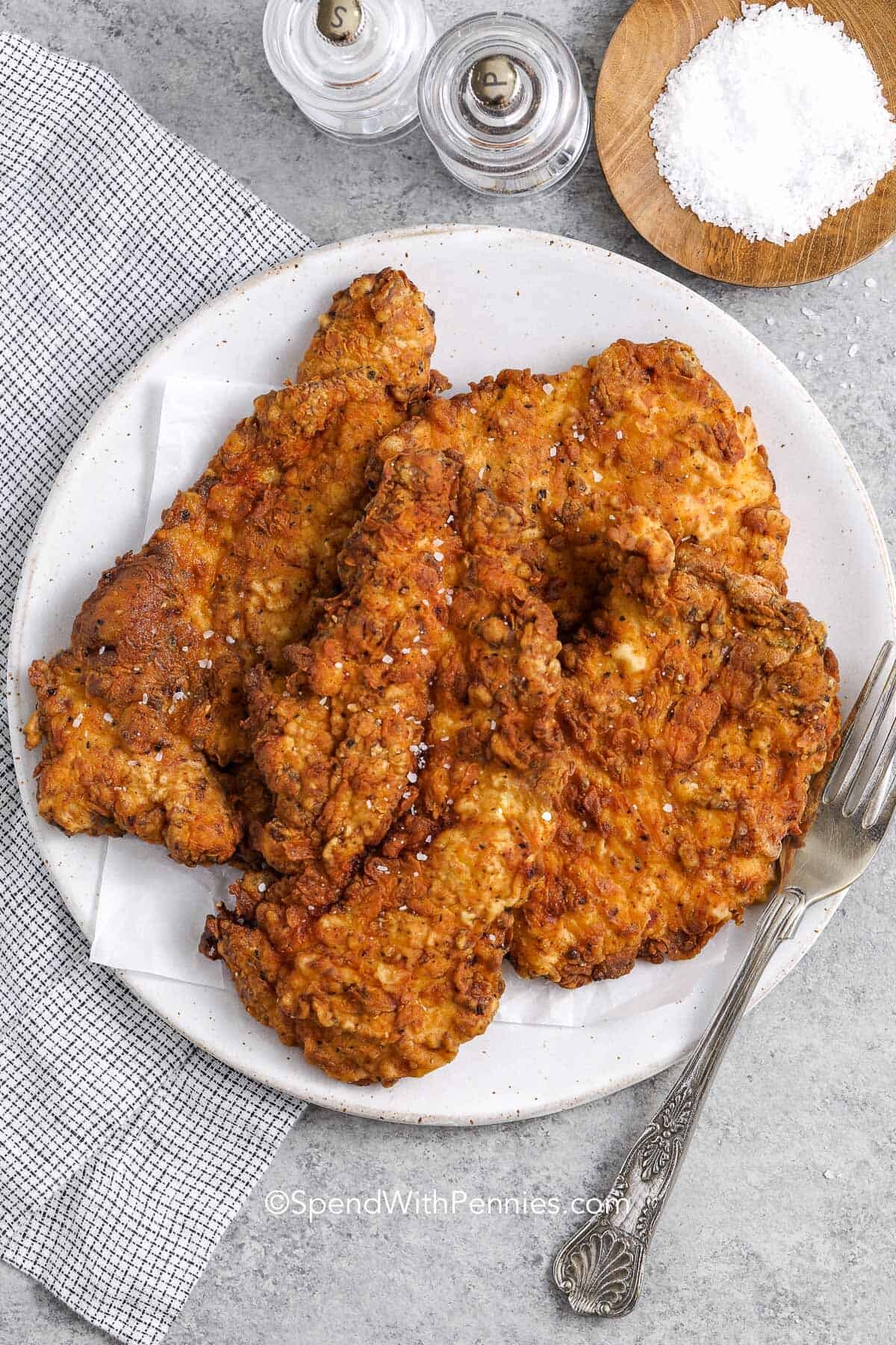 Crispy fried chicken breast on a plate next to salt