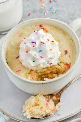 Vanilla Mug Cake with whipped cream and sprinkles with a portion taken out